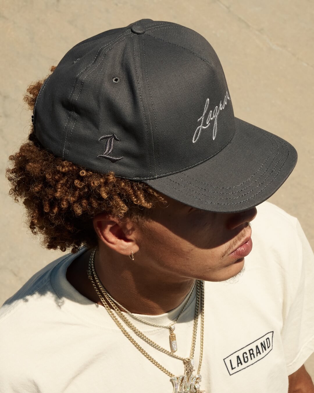 Model wearing the LAGRAND Script Hat in Cinder Grey, showing the side L embroidery